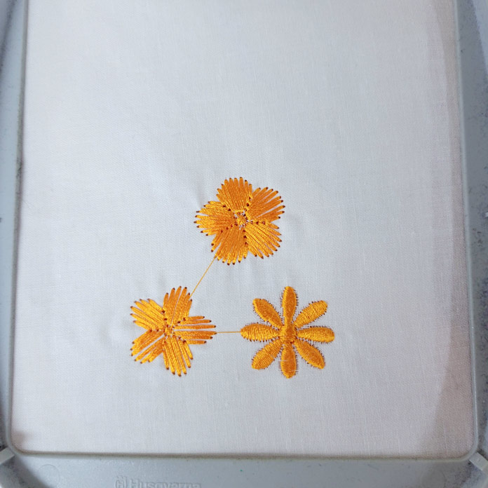 Three orange machine embroidered flowers on a white fabric; Husqvarna Viking Designer Ruby 90, Square Hoop (120mm x 120mm), Small Square Hoop (80mm x 80mm)