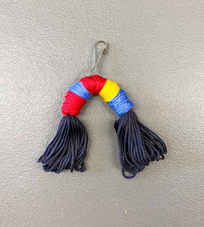 Red, blue and yellow floss wrapped around the middle of a bent skein of black floss with a clip attached in the middle; DMC Matte Cotton Yarn and Elan Snap-Clip