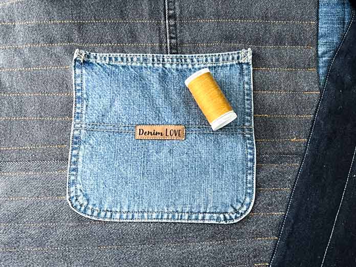 A part of the quilted quilt top shows a pocket with a Denim Love label sewn to it, and a spool of gold thread lays on top of the pocket. 
