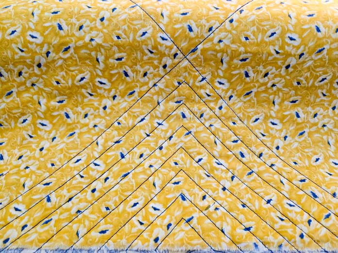 Blue lines of stitching in a chevron pattern on yellow fabric