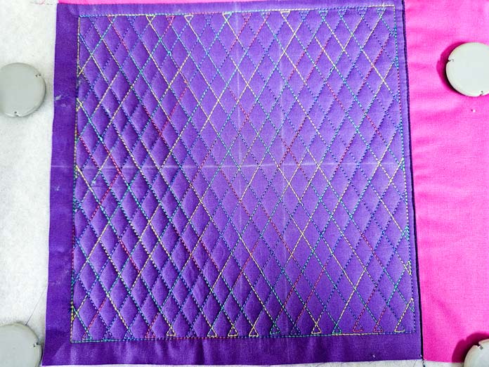 Stitching in a multi-colored thread on purple fabric; Husqvarna VIKING Quilters Metal Embroidery Hoop 200mm by 200mm