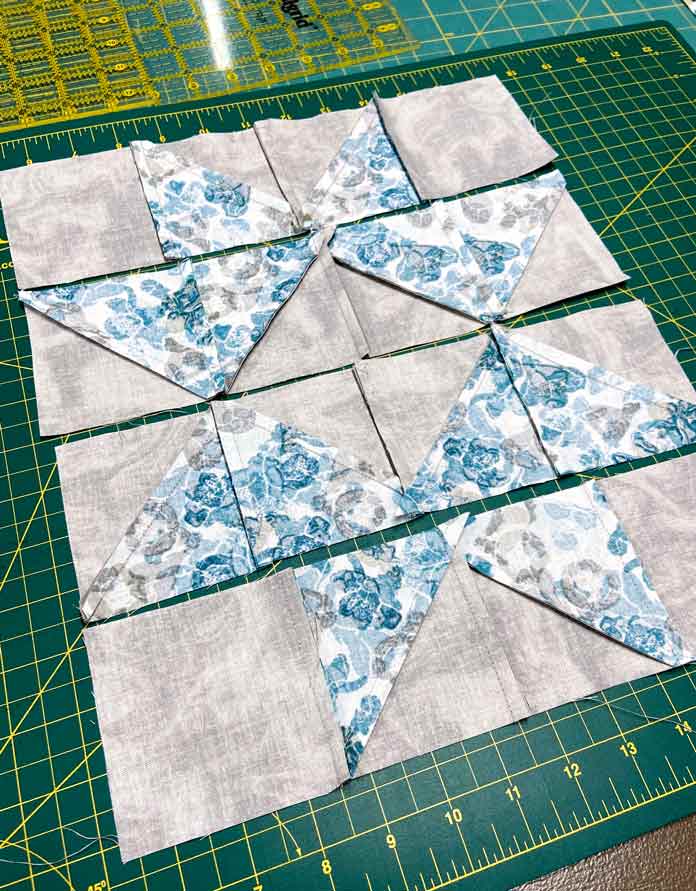 The wrong side of four rows of blue and gray HST units shown with seams pressed in opposite directions. Omnigrid Triangle Ruler for Half Square Triangles, Fabric Creations 100% Cotton Fabric, Fairfield Crafter’s Choice Pillow Form, SCHMETZ Microtex Needles, Gütermann Cotton 50wt Thread, clover Ball Point Awl, UNIQUE Wool Pressing Mat