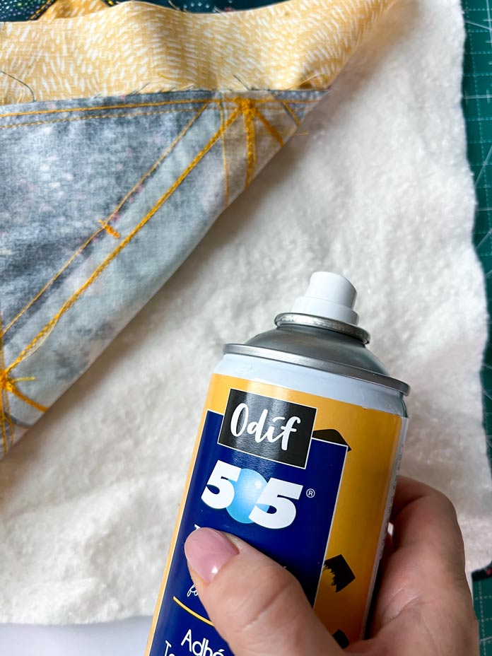 Process of layering the quilt sandwich. Ready cushion top with cotton batting and backing fabric. Hand holding the Odif temporary adhesive bottle spray