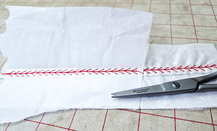 Red stitching on white fabric with metal scissors