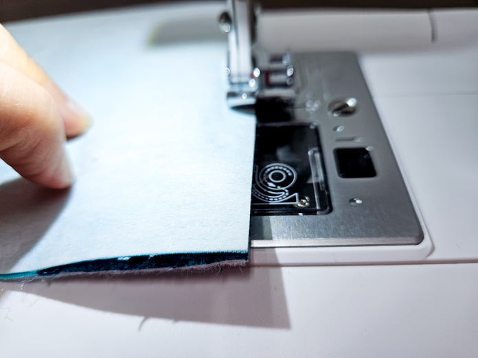 A piece of white fabric under a metal presser foot on a sewing machine