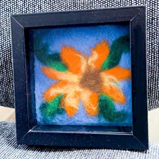 An orange and yellow flower in a black shadow box