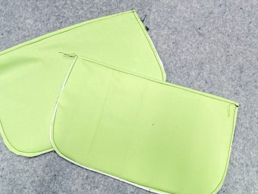 Two pockets lay on top of a grey pressing mat. The green lining is visible, and the basting stitch around the outside edge is visible.