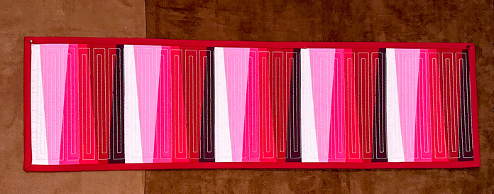 A finished and bound quilted table runner in red and pink fabrics