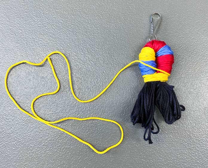 Red, blue and yellow floss wrapped around the middle of a bent skein of black floss with a clip attached in the middle, and more yellow floss is used to tie the wrapped loops; DMC Matte Cotton Yarn and Elan Snap-Clip