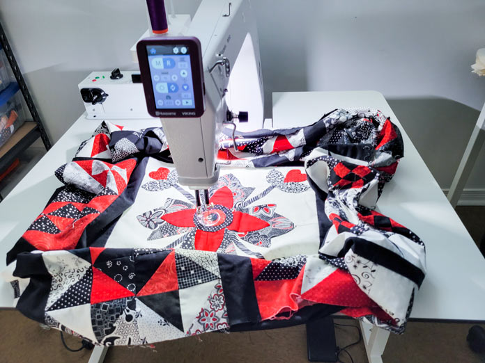 A red, white, and black quilt on a white table for a stationary quilting machine; Husqvarna Viking PLATINUM™ Q160