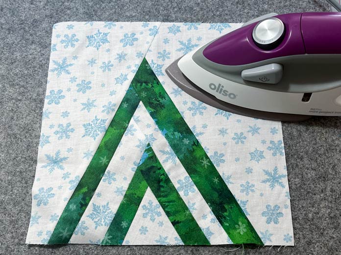The background fabric pieces are sewn to the tree and pressed with an iron on a gray wool pressing mat; Oliso M2Pro Mini Project Iron with Solemate - Orchid, UNIQUE Quilting Wool Pressing Mat - 14″ x 14″ - Grey