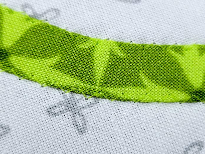 Green thread stitched onto a strip of green fabric on a white background
