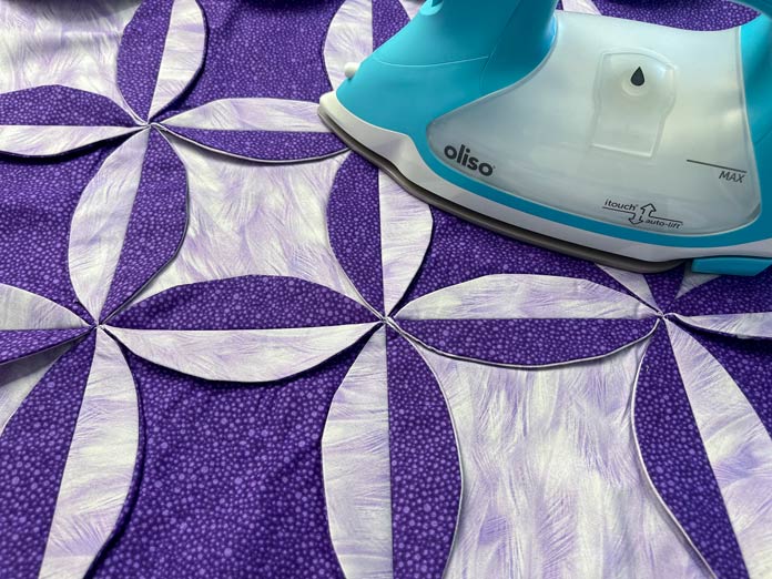 Four rows of four circles in dark purple and mauve fabrics are sewn together. The Oliso iron is used to press down the curved edges; Oliso PRO TG1600 Pro Plus Smart Iron – Turquoise