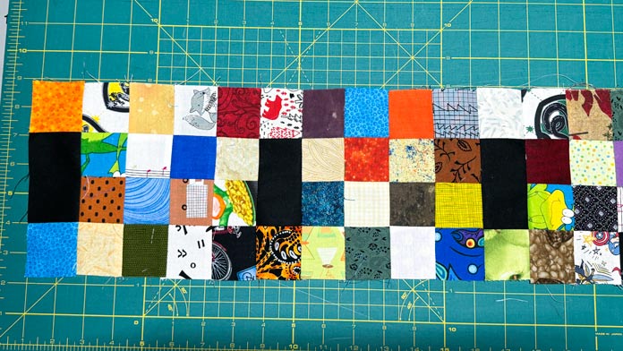 16 patch blocks with black rectangles and 2” x 2” squares are sewn to each other making a row.