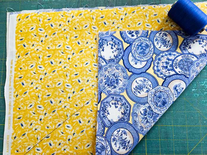 Yellow and blue fabric beside a blue fabric and a spool of blue thread