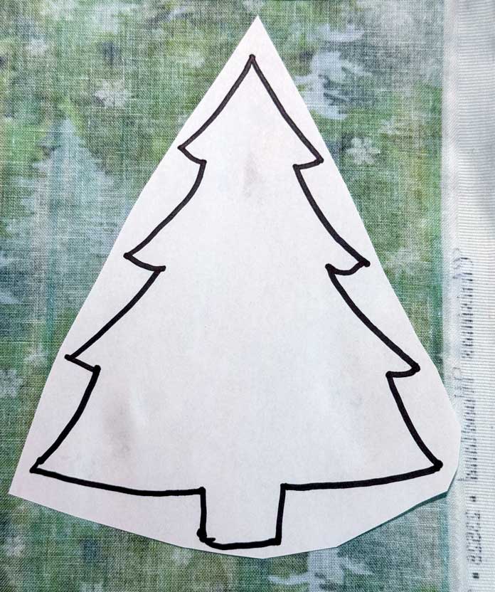 A paper Christmas tree template is placed on the wrong side of the fabric.