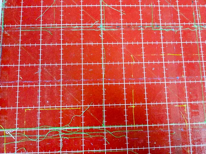 Green threads on a red digital cutter mat