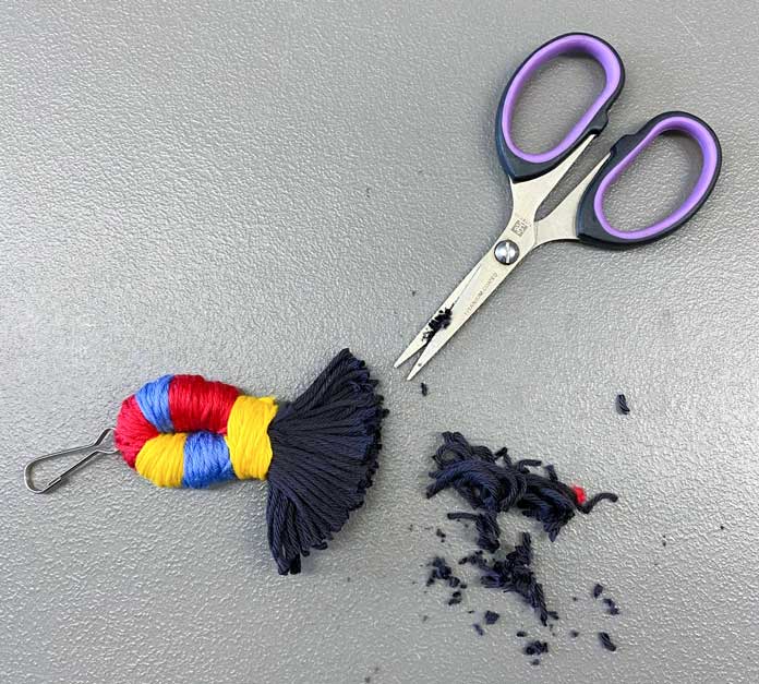 A finished red, blue, and yellow tassel that has been trimmed with scissors; DMC Matte Cotton Yarn and Elan Snap-Clip