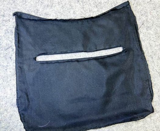 A piece of black purse lining with a slit cut horizontally in the middle sits on a grey pressing mat