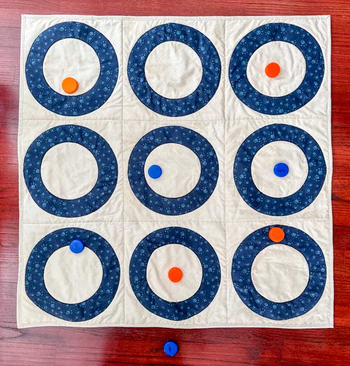 The completed quilt with nine rings, some containing objects to mark scores.