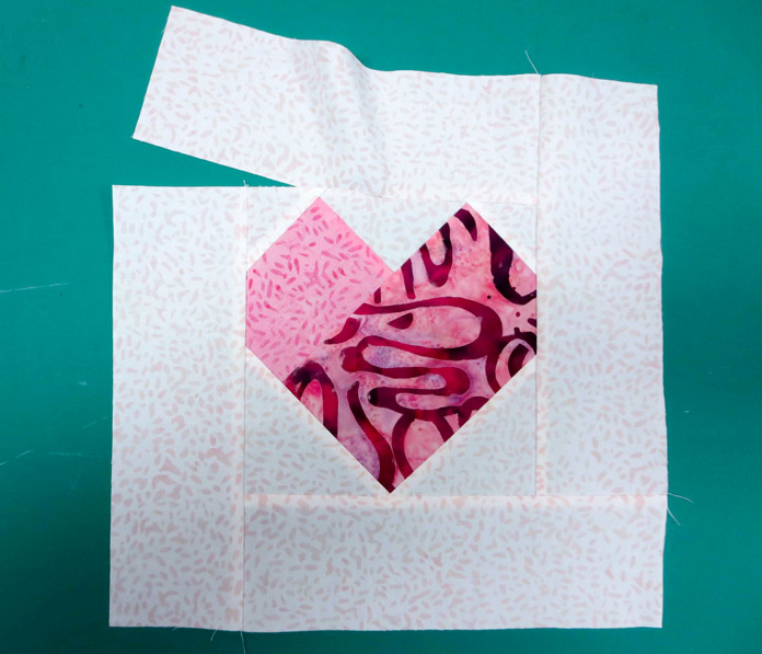 A red and pink pieced heart on a white background with a partial seam on the top border.