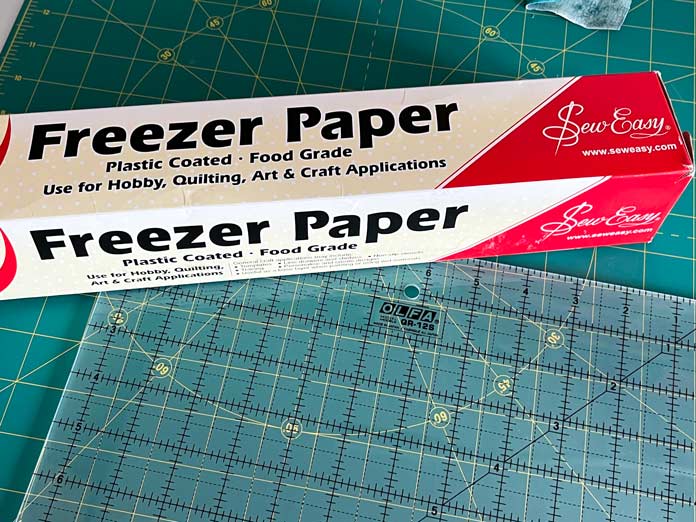 Sew Easy Freezer paper and OLFA’s 12½” x 12½” ruler laid out on a cutting mat; OLFA 12.5″ Square Frosted Acrylic Ruler, OLFA 6″ x 12″ Frosted Acrylic Ruler, OLFA 6″ x 24″ Frosted Acrylic Ruler, OLFA Square Rotating Cutting Mat, Sew Easy Freezer Paper for Quilting and Applique - 12.1m x 38.1cm (13.2yd x 15″)