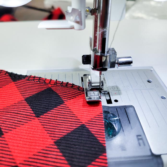 Red and black fabric under a metal presser foot on a sewing machine; Husqvarna Viking Tribute 150C