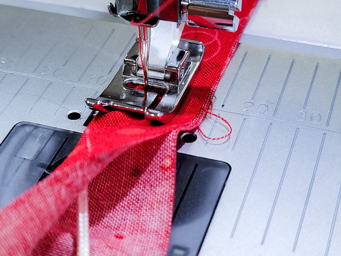 Red fabric with a white cord inside under a sewing machine presser foot; Husqvarna Viking Tribute 150C