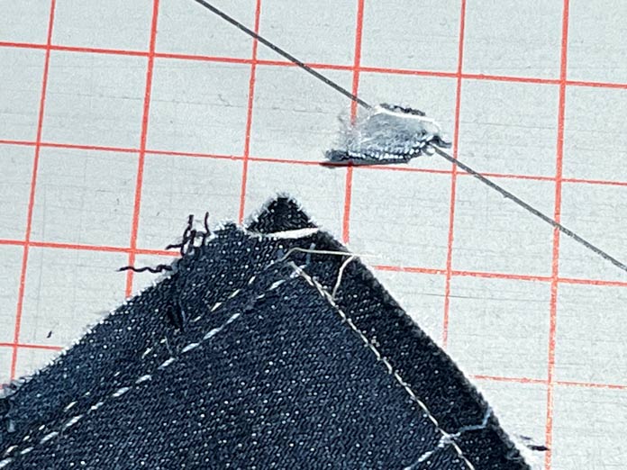 A close-up of a piece of denim fabric with the corner snipped off.