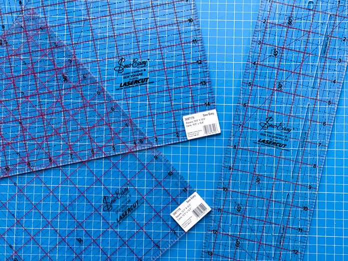 The Sew Easy 121⁄2″ x 121⁄2″, 151⁄2″ x 151⁄2″ and 14″ x 41⁄4″ rulers on a blue Heirloom cutting mat.
