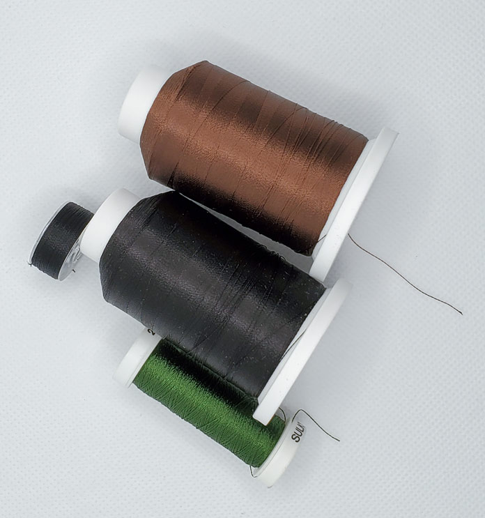 A pre-wound bobbin with black thread, a small spool of green thread, and a larger spool of black and brown thread