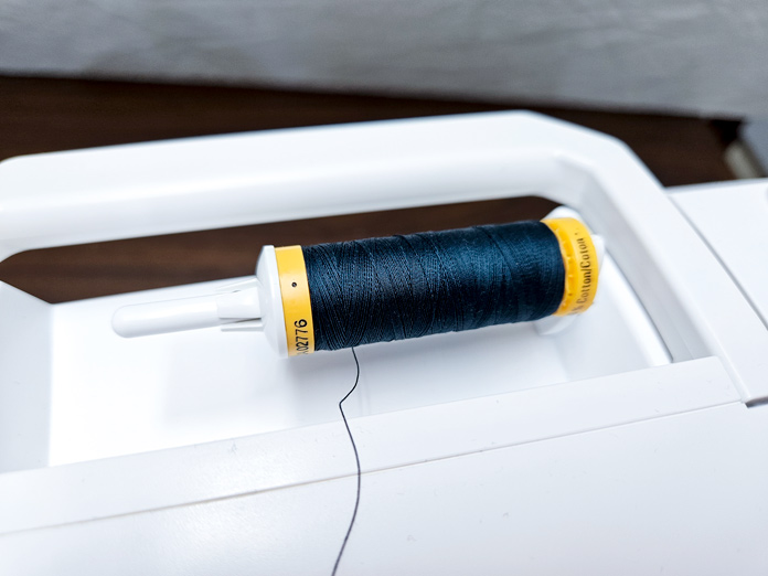 A spool of dark thread on a white sewing machine