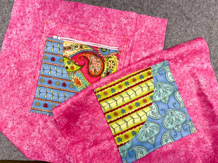 Two pink lining fabrics with multicolored pockets are shown lying on top of each other on a grey pressing mat.