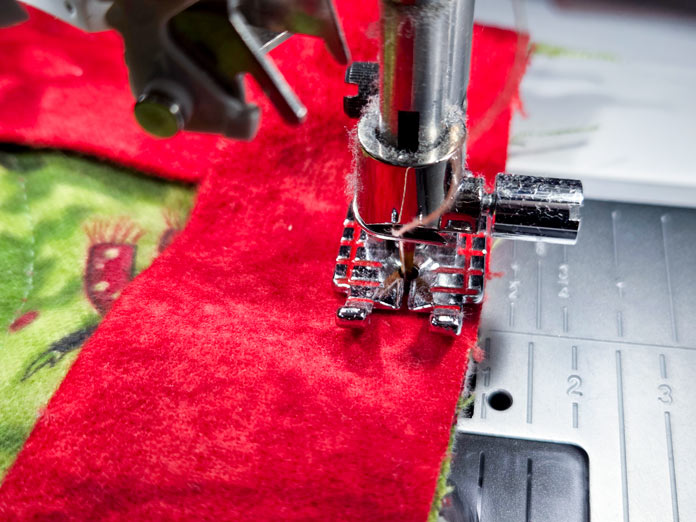 A metal presser foot stitching red fabric to green fabric