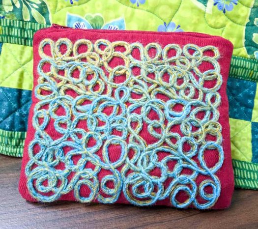 A red zippered pouch with blue and green yarn