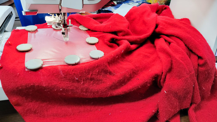 A red sweater hooped in a metal hoop on an embroidery machine