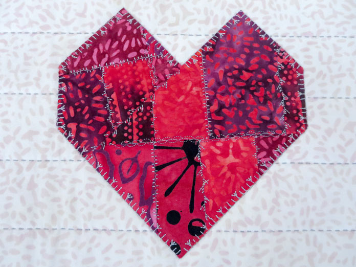 A variety of new decorative stitches on the red pieced heart shape and hand-quilting stitches on the background fabric.