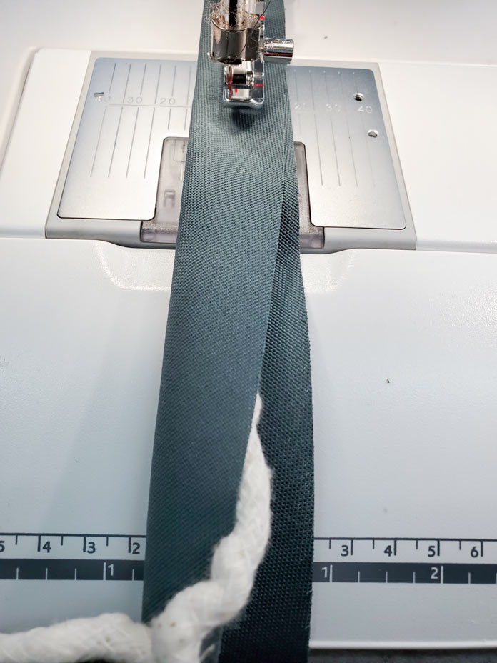 A strip of green fabric with a piping cord inside stitched on a sewing machine