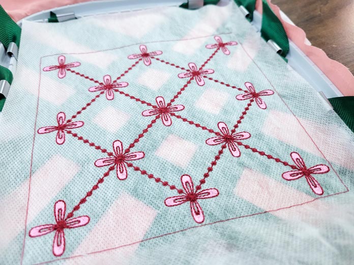 Pink flowers and burgundy lines on a layer of white fabric with green ribbons showing; Husqvarna Viking Texture Hoop, Inspira Aqua Magic stabilizer