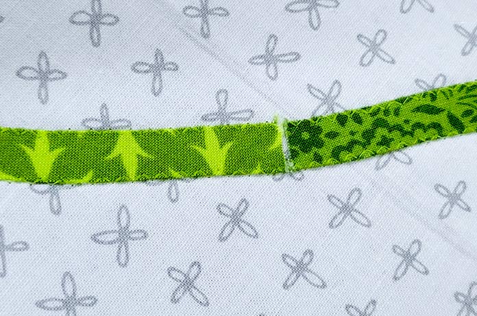 A light green thread stitched on two different strips of green fabric on white fabric