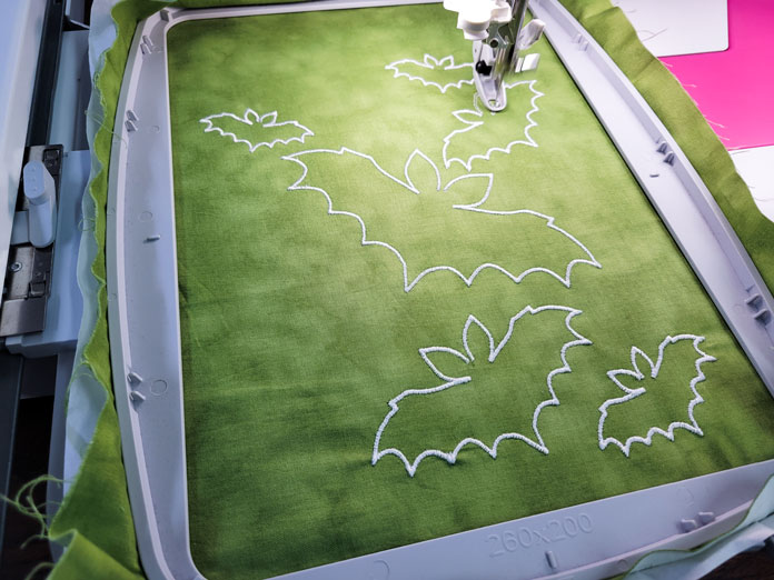 White outlines of bats on green fabric in a machine embroidery hoop; Husqvarna Viking Designer EPIC 2