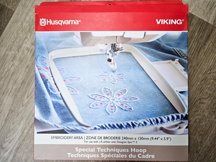 A red box with a picture of a blue fabric in a machine embroidery hoop; Husqvarna VIKING DESIGNER EPIC 3