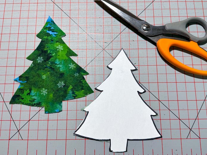 A fabric Christmas tree shape is cut from a paper template using a pair of Infiniti scissors.