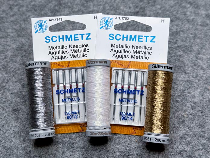 Two packages of SCHMETZ metallic needles sizes 80/12 and 90/14 and three spools of Gütermann metallic thread, silver, white, and gold; Gütermann Dekor Metallic Thread 200m – Gold, Gütermann Dekor Metallic Thread 200m - Col. 41, Gütermann Dekor Metallic Thread 200m – Red, Gütermann Dekor Metallic Thread 200m - Christmas Green, Gütermann Dekor Metallic Thread 200m - Col. 1005, Gütermann Denim Thread 100m – Black, UNIQUE Baby Rick Rack 3mm x 3.7m – Scarlet, UNIQUE Medium Rick Rack 6mm x 2.3m - Emerald Green, UNIQUE Jumbo Rick Rack 10mm x 2.3m - Metallic Gold, SCHMETZ #1743 Metallic Needles Carded - 80/12 - 5 count, SCHMETZ #1752 Metallic Needles Carded - 90/14 - 5 count, LDH 8½“ Craft Scissors – Purple, HeatnBond Lite Iron-On Adhesive - 43cm x 30m (17″ x 32 ¾yds) bolt, HeatnBond Stitch n Sew Tear-Away Stabilizer - 50.8cm x 22.8m (20″ x 25yds), oliso M3Pro Project Iron – Coral, OLFA 45mm RTY-2/DX/MAG Ergonomic Rotary Cutter – Magenta, UNIQUE Quilting Wool Pressing Mat - 18″ x 24″ - Grey