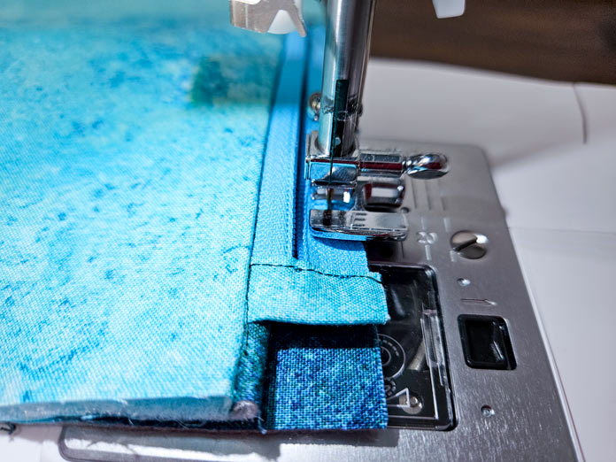 A blue zipper under a metal presser foot on a sewing machine