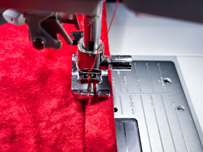 A metal presser foot sewing red fabric