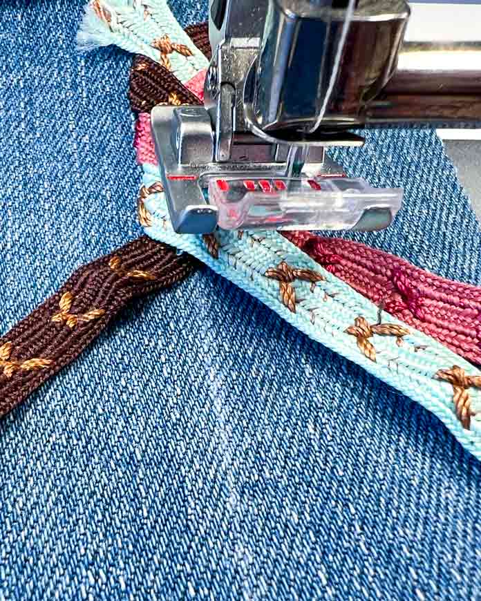 Folding the third (teal) ribbon over the first (brown) and aligning it in front of the needle—parallel to the second (pink) ribbon—marks the beginning of a new circle in the Triple Ribbon Stitch braid pattern on the PFAFF creative icon 2. 