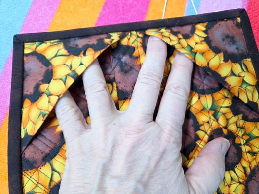 A hand and two squares of yellow and brown fabric