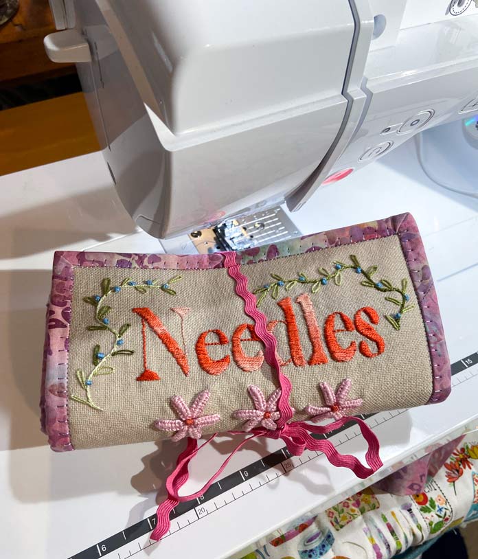 The rolled and tied up embroidered fabric needle roll sitting on the extension table of the sewing machine.