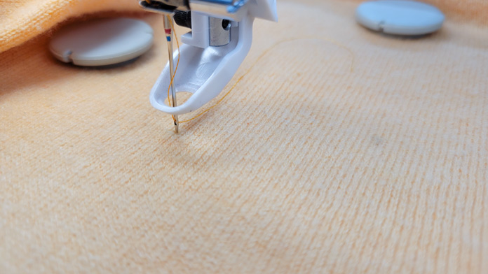 A needle and machine embroidery presser foot on an orange sweater; Husqvarna Viking Designer Ruby 90